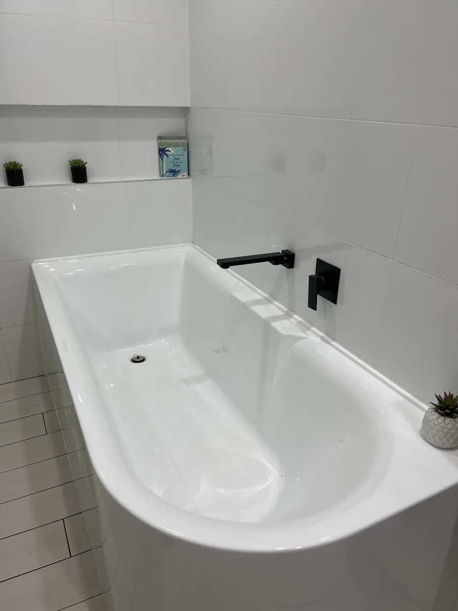White back-to-wall bath with matte black tapware in a freshly tiled bathroom