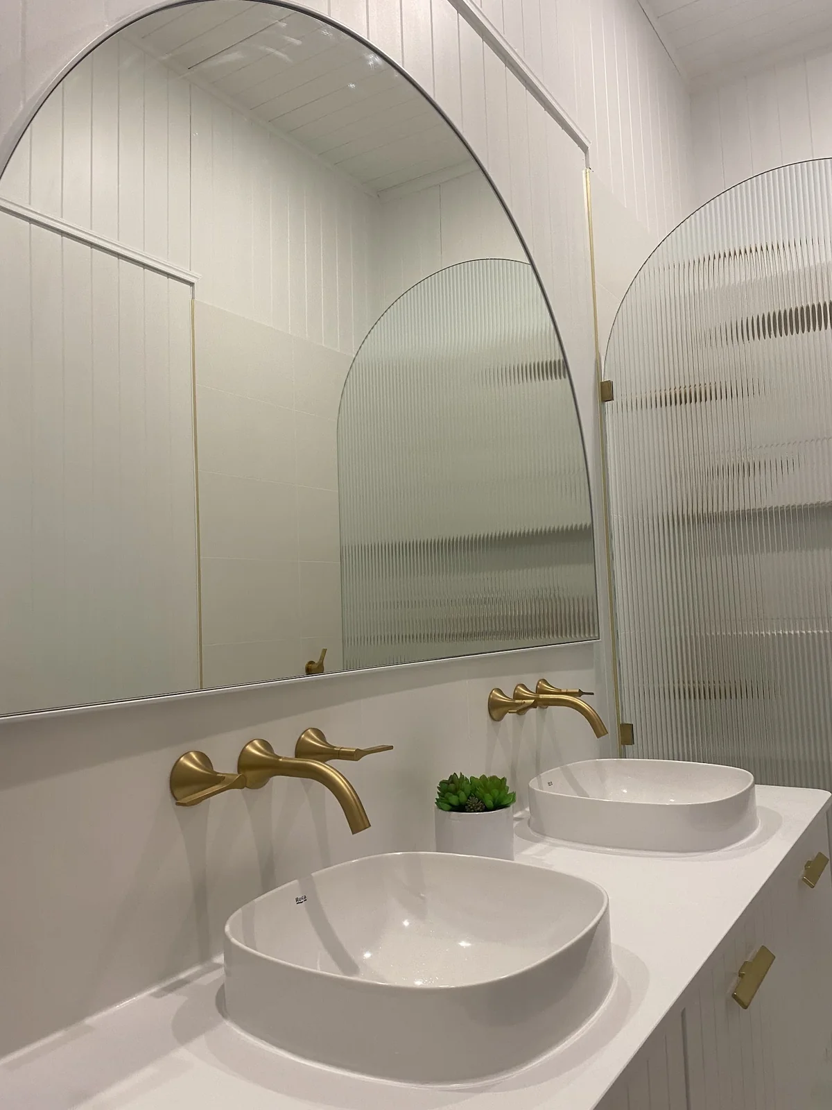 Double vanity with vessel basins, brushed brass wall mixers and an arched mirror