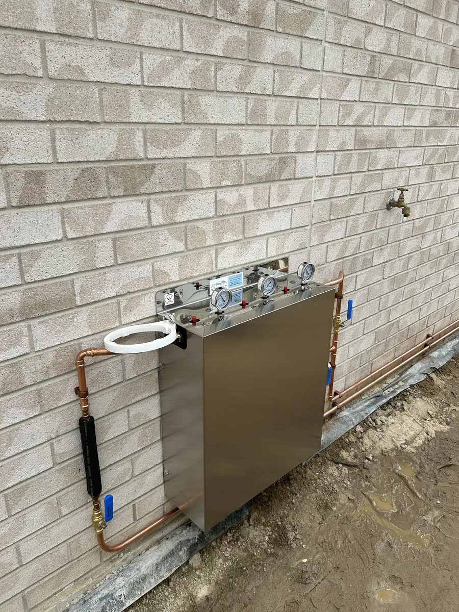 Stainless steel unit with gauges and new copper pipework on an exterior brick wall